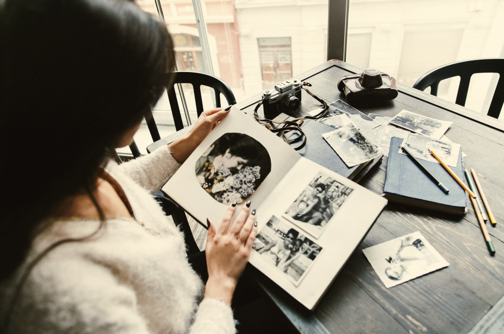 Junge Frau sitzt am Tisch und blättert durch ein altes Fotoalbum als Symbolbild für den Beitrag: Früher war alles besser, oder?