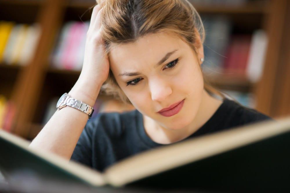 Eine Frau liest angestrengt ein Buch als Symbolbild für Lesefrust.
