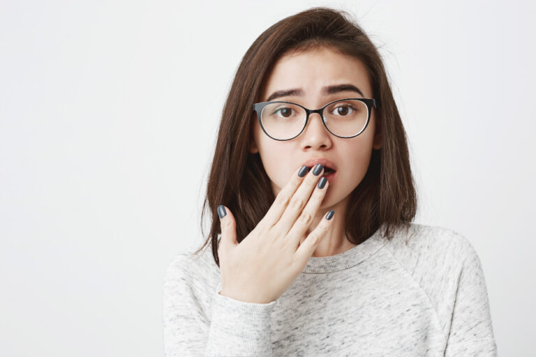 Eine Frau mit Brille hält erschrocken ihre Hand vor geöffnetem Mund als Symbolbild für Ratgeber: Mit Herpes zum Zahnarzt
