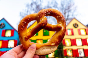 Eine Brezel in die Luft gehalten vor einer bunten Häuserkulisse als Symbolbild für den Beitrag: Wie viel Kalorien hat eine Brezel?