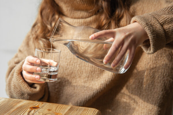 Eine Frau gießt sich Wasser aus einer Karaffe in ein Glas ein als Symbolbild für Ratgeber: ständig Durst trotz Trinken