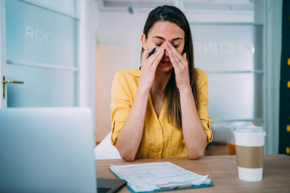 Junge Frau im Büro hat Kopfschmerzen von zu viel Koffein