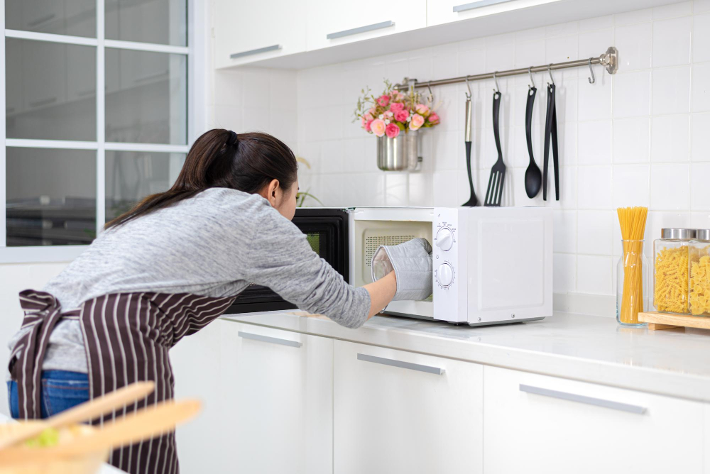 Frau steht an einer geöffneten Mikrowelle als Symbolbild für Reis in der Mikrowelle kochen