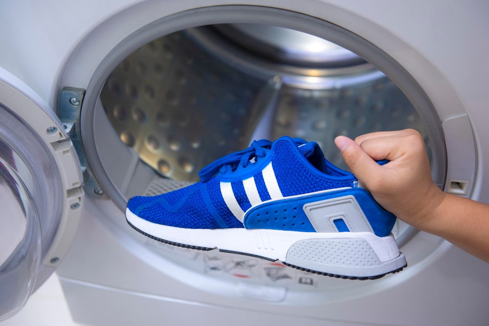 Hand hält Schuhe vor die Waschmaschinen-Trommel - ist es sinnvoll Schuhe in der Waschmaschine zu waschen und wenn ja, wie?