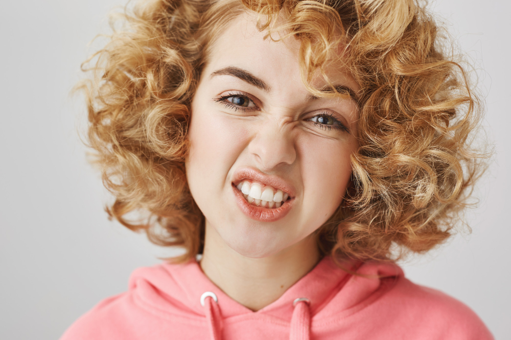 Junge Frau sieht verschmitzt in die Kamera und zeigt dabei ihre Zähne als Symbolbild für den Beitrag: Weiße Flecken auf den Zähnen: Kann man was tun?
