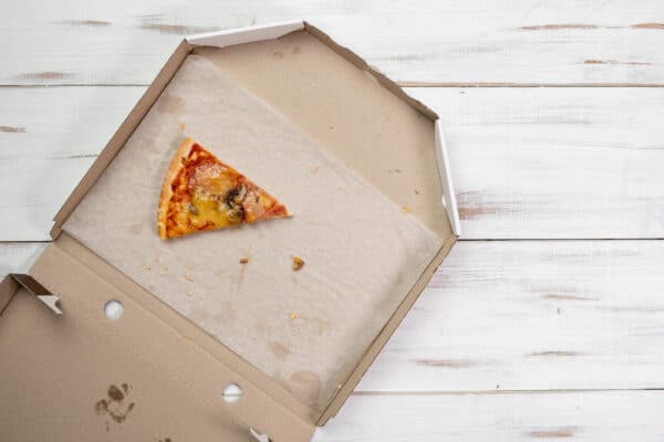 Geöffneter Pizzakarton mit nur noch einem Stück Pizza als Symbolbild für den Ratgeber: Pizzakarton entsorgen