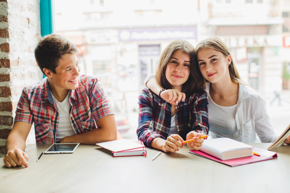 2 Mädchen und ein Junge sitzen gemeinsam vor Schulsachen in der Schule als Symbolbild für den Beitrag: Was ist eine Sekundarschule?