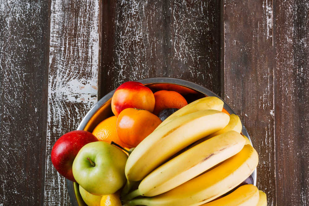 Äpfel, Bananen und andere Früchte in einer Obstschale auf einem Holztisch von oben aufgenommen als Symbolbild für den Ratgeber: Quetschies selber machen