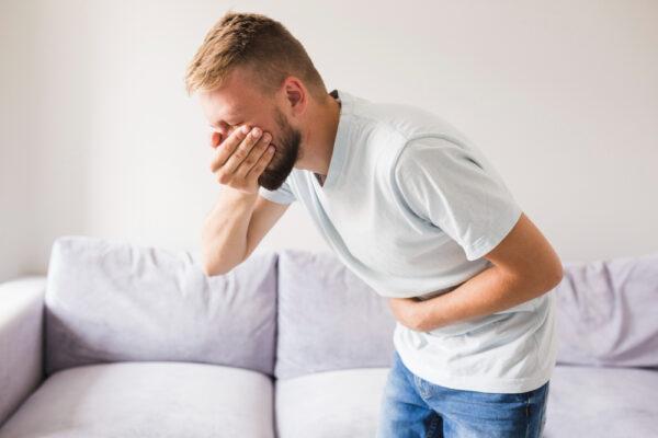 Ein Mann hält sich den Bauch und gleichzeitig den Mund zu als Symbolbild für Ratgeber: Erbrechen trotz leerem Magen