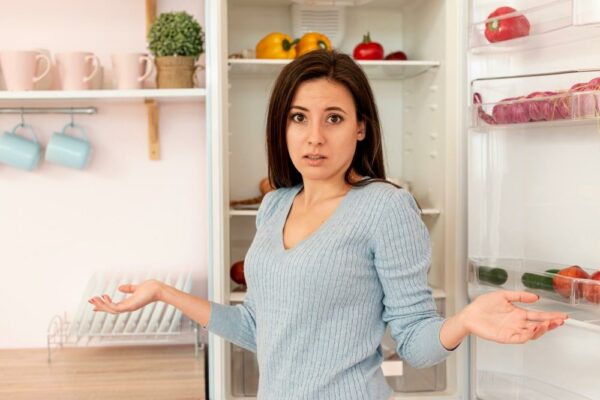 Frau steht fragend vor dem Kühlschrank - symbolisch für die Frage wie man diesen entsorgen kann
