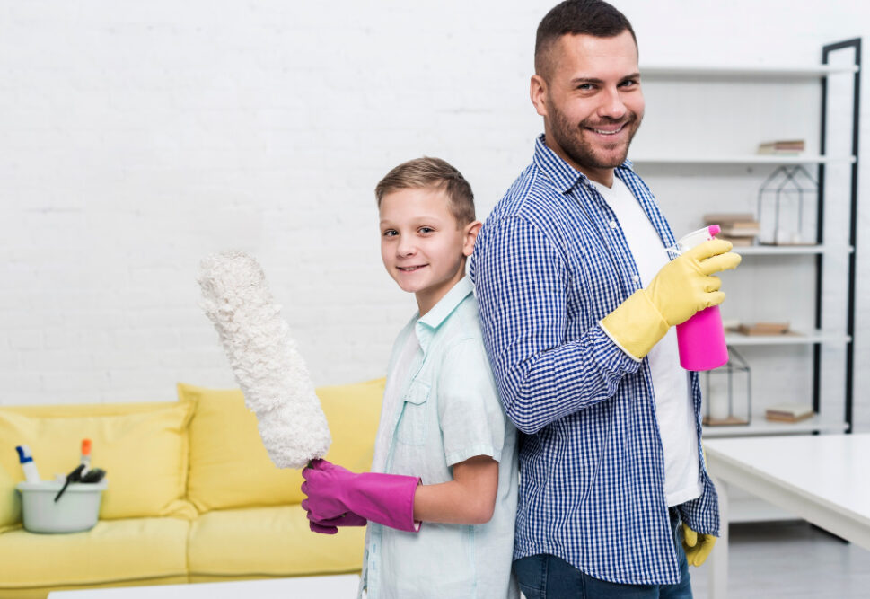 Vater und Sohn Rücken an Rücken mit Putzmitteln in der Hand als Symbolbild für den Ratgeber: Putzplan für die Familie