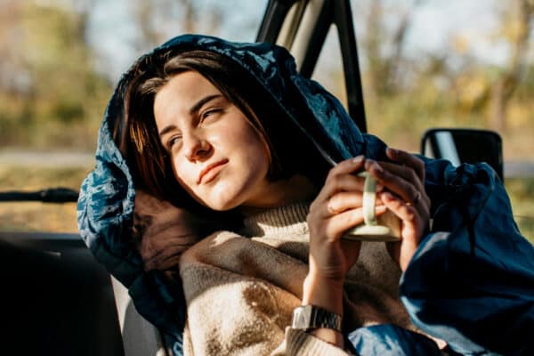 Junge Frau lehnt sich zurück und genießt unterwegs einen Kaffe als Symbolbild für den Ratgeber: Slow Travel als umweltschonende Alternative