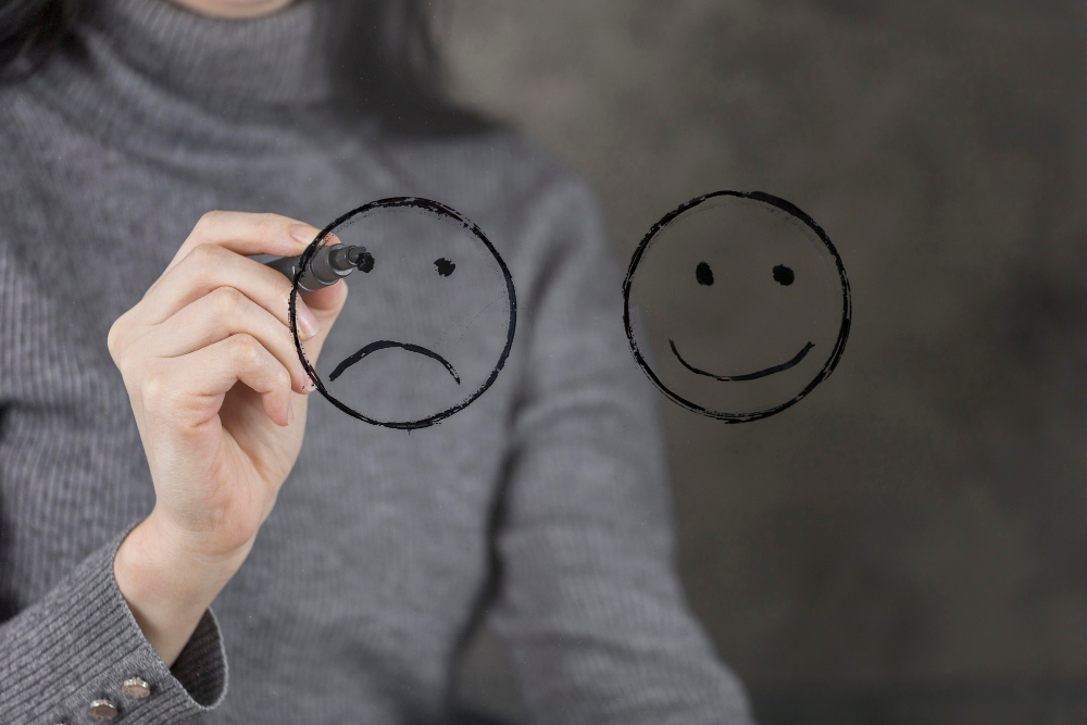 Frau malt einen traurigen Smiley auf eine Glasscheibe als Symbolbild für den Ratgeber: Emotionale Vernachlässigung Folgen im Erwachsenenalter