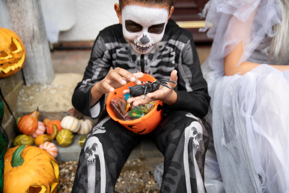 Junge verkleidet als Skelett wirft einen Blick auf gesammelte Sußigkeiten zu Halloween