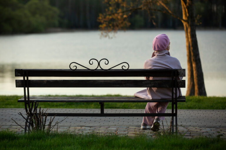 Alte Frau sitzt alleine auf der Parkbank am See als Symbolbild für den Ratgeber: Wieviel Witwenrente bekomme ich, wenn ich selber Rente bekomme?
