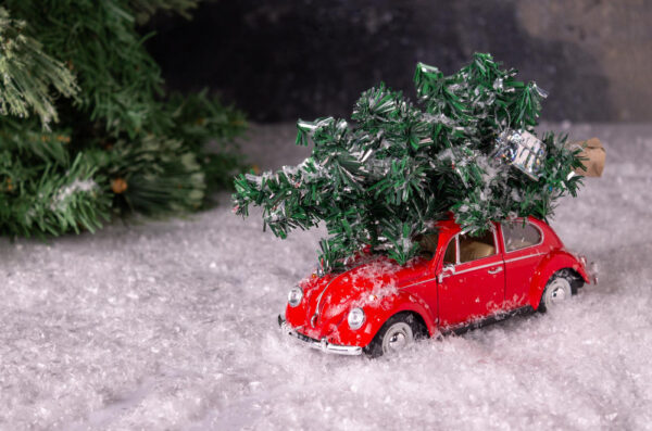 Spielzeugauto auf Kunstschnee mit einem Bäumchen auf dem Dach als Symbolbild für den Ratgeber: Weihnachtsbaum transportieren