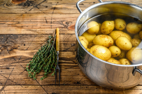 Kartoffeln mit Schale im Topf voll Wasser neben Küchenkräutern