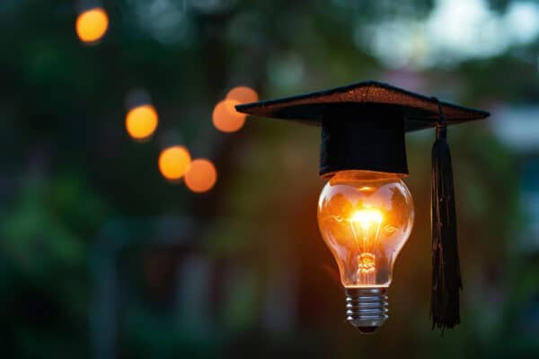 Eine glühende Glühlampe unter einem Mortarboard - Symbolbild für den Leitfaden zur Bachelorarbeit