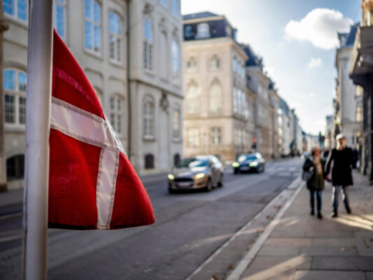 Autos auf der Straße, im Vordergrund eine dänische Flagge (Symbolbild für: Mit dem Auto nach Dänemark)