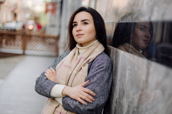 Frau lehnt an einer Hauswand und schweift mit ihrem Blick gedankenversunken Richtung Himmel als Symbolbild zum Ratgeber: Warum manche Frauen keinen Partner finden.