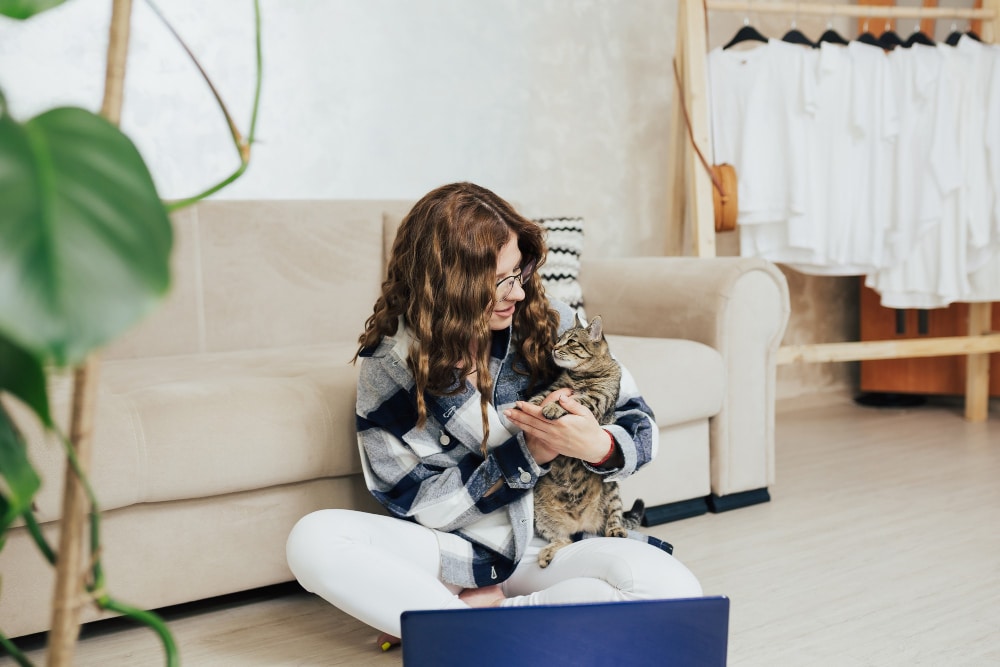 Frau sitzt im WOhnzimmer vor der Couch auf dem Boden und spielt mit einer Katze als Symbolbild für den Ratgeber: Darf der Vermieter Haustiere eigentlich verbieten?