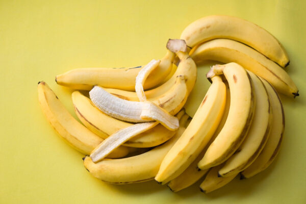 Viele Bananen auf gelbem Hintergrund und eine ist geöffnet als Symbolbild für den Ratgeber: Banane gegen Durchfall