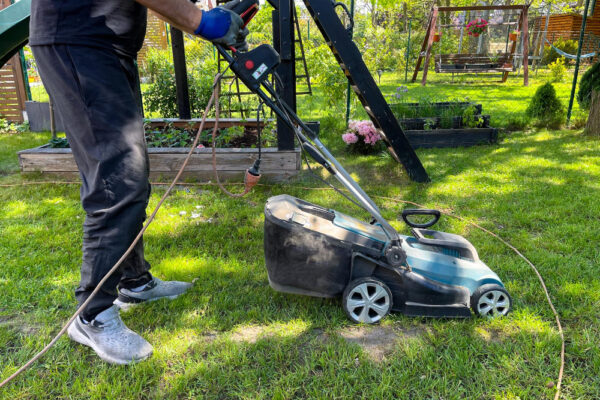 Mann führt einen Rasenmäher übers Gras als Symbolbild für den Ratgeber: Darf man sonntags Rasen mähen