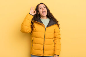 Frau in Daunenjacke zeigt "Alles Ok" als Symbolbild für den Ratgeber Daunenjacke trocknen