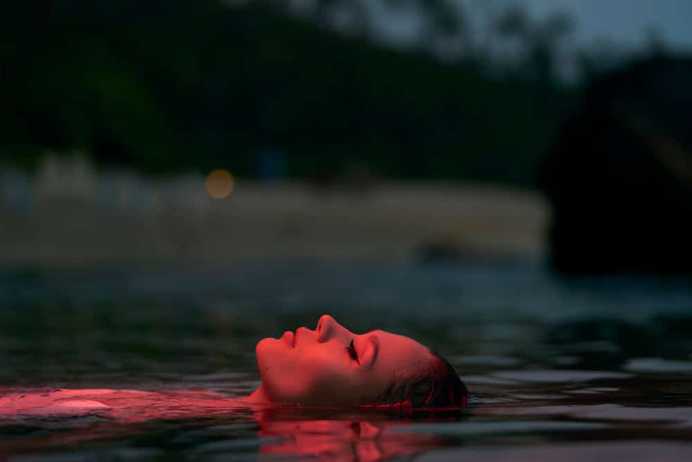 Frau genießt ruhiges Schwimmen in der Lagune in der Abenddämmerung als Symbolbild für den Ratgeber: Meditation zum Einschlafen