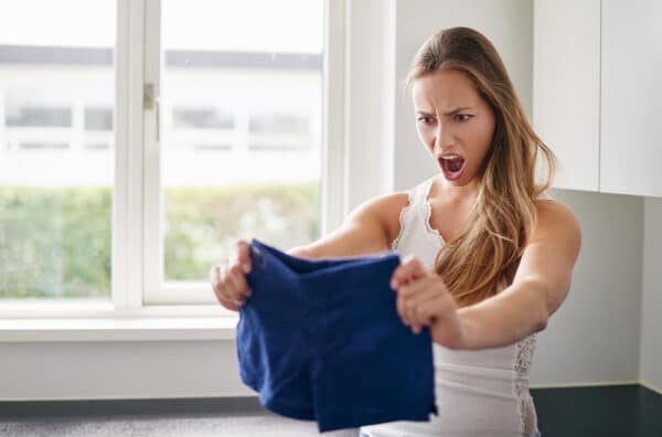 Junge Frau hält eine Hotpants in den Händen und stellt fest, dass diese eingelaufen ist als Symbolbild für den Ratgeber: Eingelaufene Kleidung retten