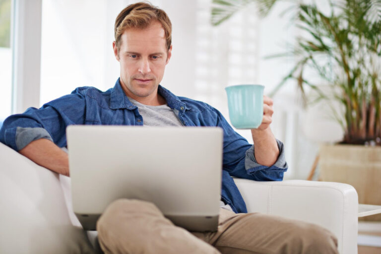 Mann am Laptop auf der Couch mit einer Tasse Kaffee in der Hand als Symbolbild für den Ratgeber: Opodo Prime kündigen