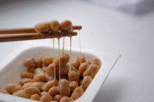 Natto wird mit Stäbchen aus einer Schale geholt als Symbolbild für den Beitrag: Was ist Natto und wie stellt man es her?