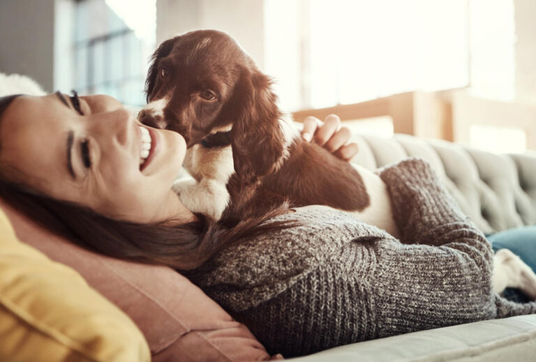 Hund leckt liegende Frau auf dem Sofa ab