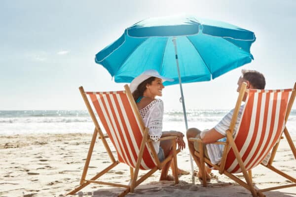 Päärchen sitzt am Strand unterm Sonnenschirm - symbolisch für wichtige Versicherungen für eine Auslandsreise