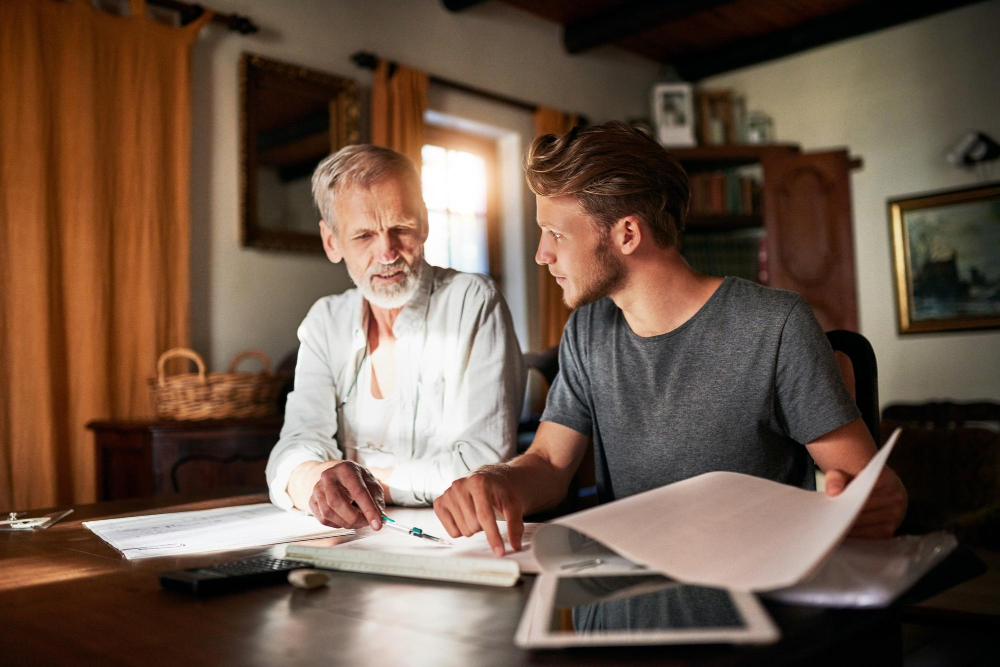 Vater und Sohn sitzen am Tisch vor Papierkram - Symbolbild für das Thema Schenkung an Kinder zu Lebzeiten