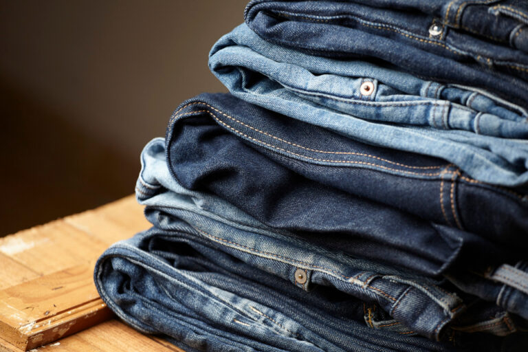 Ein Stapel verschiedener Jeans auf einer Holzkiste als Symbolbild für den Ratgeber: So findest du die perfekte Jeans