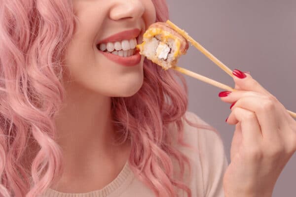 Junge Frau isst Sushi mit Stäbchen