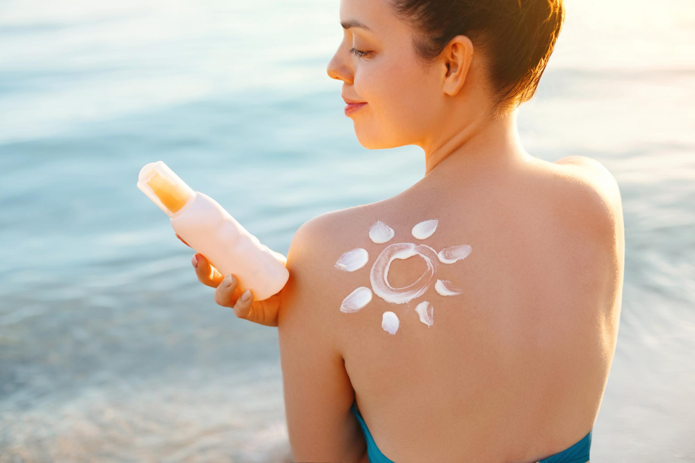 Junge Frau hält eine Flasche Sonnencreme in der Hand und auf ihrer Schulter ist eine Sonne aus Creme zu sehen als Symbolbild für den Ratgeber: Wie lang ist Sonnencreme haltbar