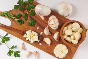 Petersilie und Knoblauch in verschiedenen Verarbeitungsstufen auf einem Holzbrett als Symbolbild für Ratgeber: frischen Knoblauch lagern