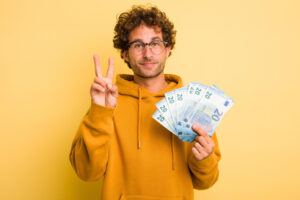Mann hält ein paar 20 € Scheine in der Hand und zeigt mit der anderen Hand ein Peace-Zeichen als Symbolbild für den Ratgeber: Payback Punkte auszahlen