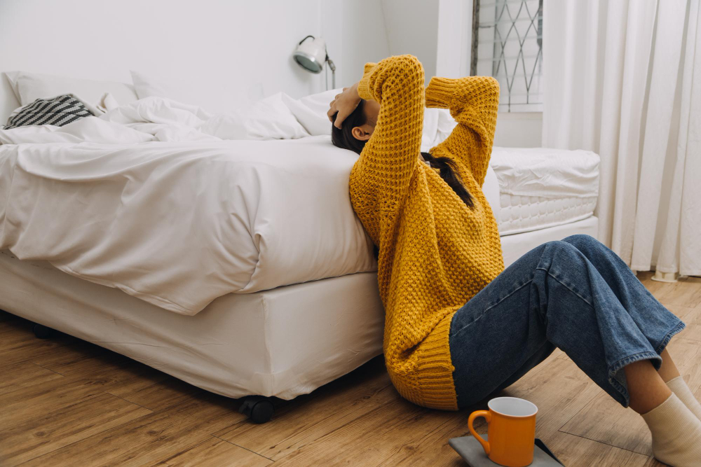 Eine Frau die i Schlafzimmer auf dem Boden sitzt und sich an den Kopf greift als Symbolbild für Ratgeber: Pollen in der Wohnung