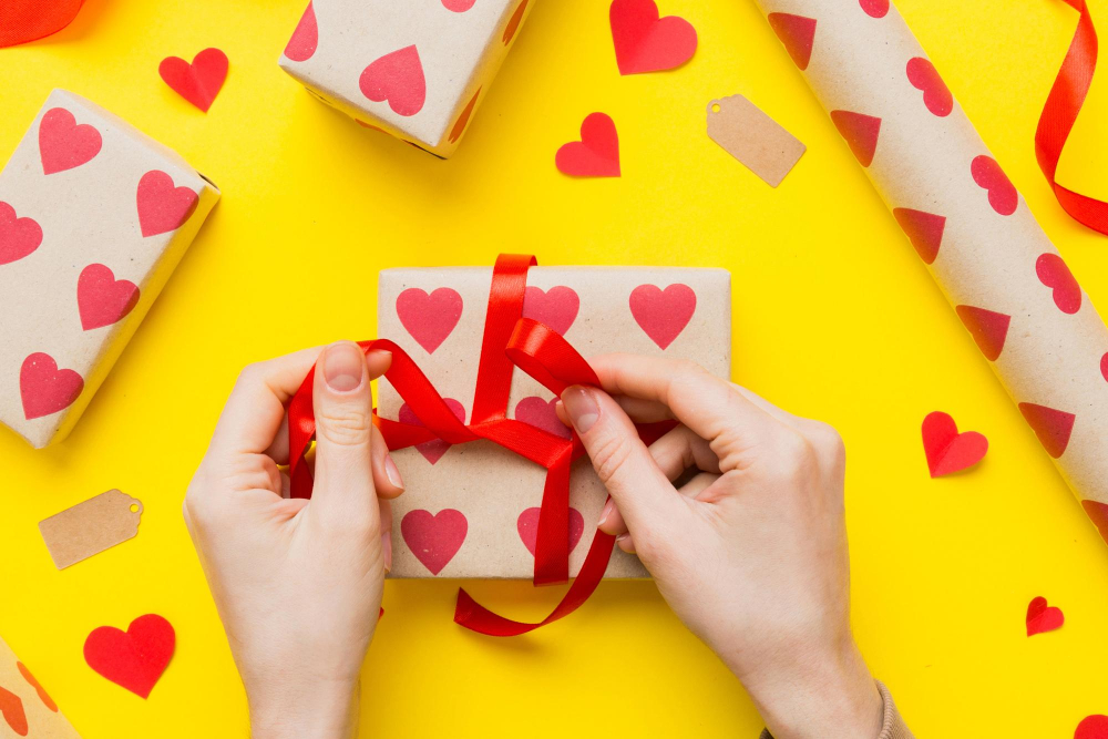 Zwei Hände verpacken ein Geschenk in Kraftpapier mit Herzchen bedruckt als Symbolbild für für den Ratgeber: Lustige Geschenke für Männer selber machen