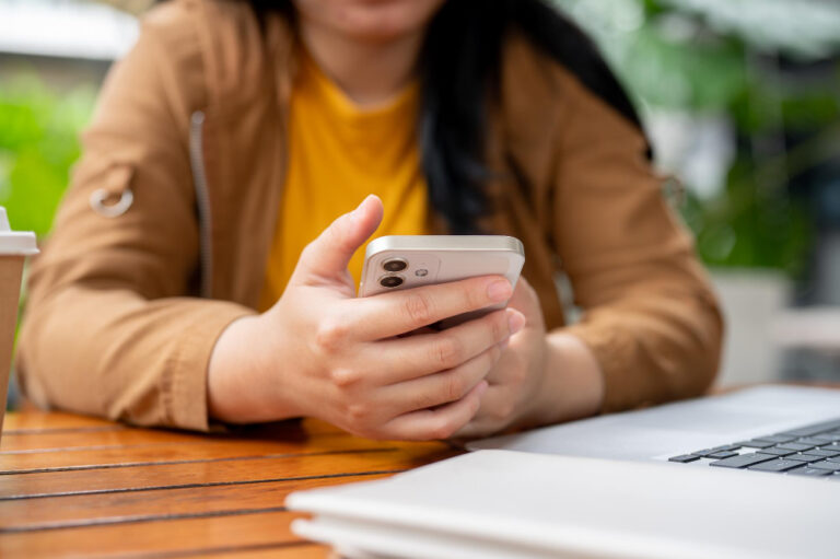 Frau sitzt am Tisch und scrollt am Smartphone als Symbolbild für den Ratgeber: Sieht man Screenshots bei Instagram Story