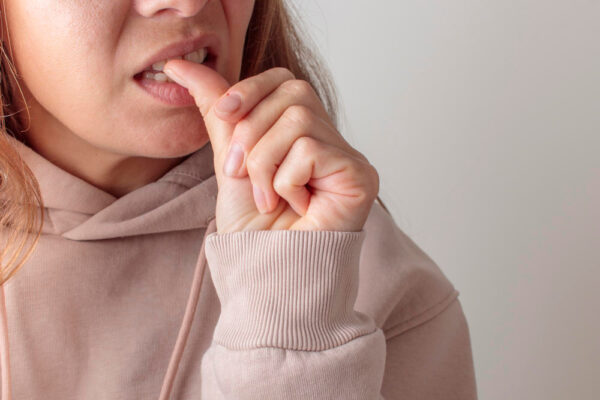 Junge Frau, die ihren Daumen gegen einen Zahn drückt, symbolisch für Zahnschmerzen und was dagegen hilft