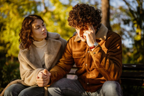 Junges Paar sitzt im Wald und scheint zu diskutieren als Symbolbild für den Ratgeber: Wenn der Partner Entscheidungen alleine trifft