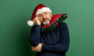 Mann mit Weihnachtsmütze vor einem grünen Hintergrund sieht fragend aus als Symbolbild für den Ratgeber: Wann wünscht man Frohe Weihnachten?