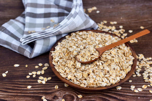 Ein Teller voll Haferflocken neben einem blau.weiß-kariertem Küchenhandtuch auf einem Holztisch als Symbolbild für den Ratgeber: Warum keine Haferflocken bei Fructoseintoleranz?