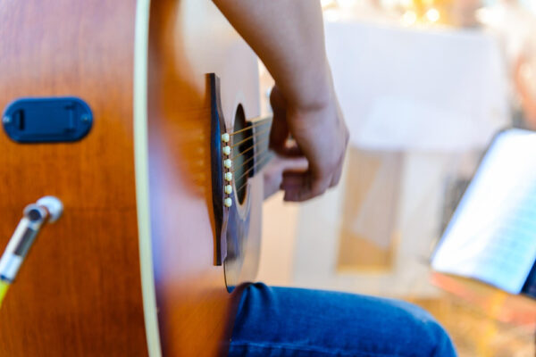 Nahaufnahme einer Person, die eine Akustikgitarre spielt. Eine großartige Aktivität, die man alleine zu Hause üben kann, um neue Fähigkeiten zu erlernen und kreative Auszeit zu genießen.