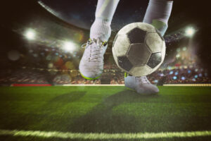 Blickwinkel auf die Füße eines Fußballers, der einen Fußball kickt als Symbolbild für den Beitrag: Wie lange geht ein Fußballspiel?