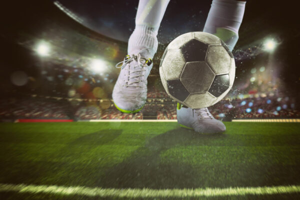 Blickwinkel auf die Füße eines Fußballers, der einen Fußball kickt als Symbolbild für den Beitrag: Wie lange geht ein Fußballspiel?